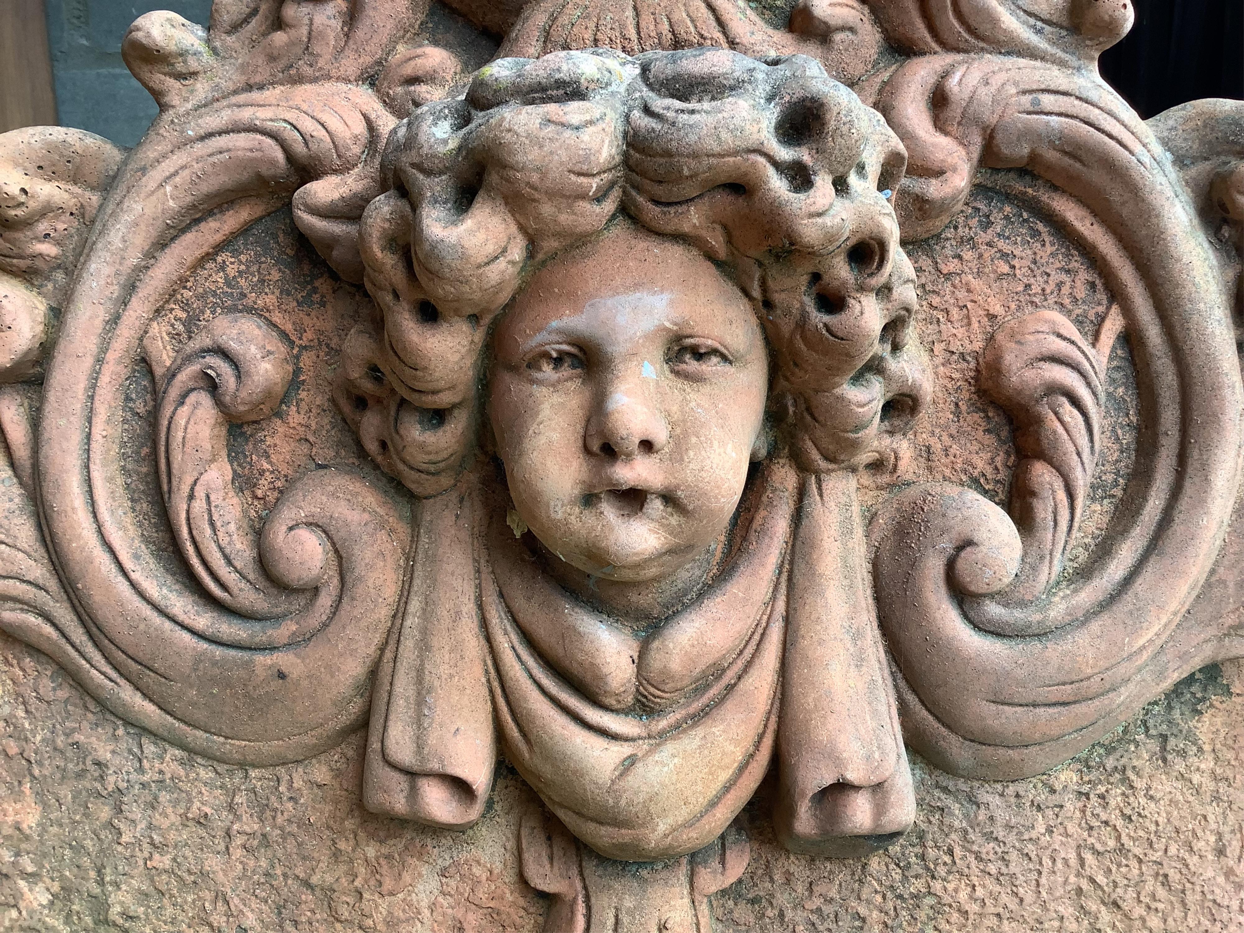 A terracotta cherub head garden wall plaque, width 54cm, height 54cm